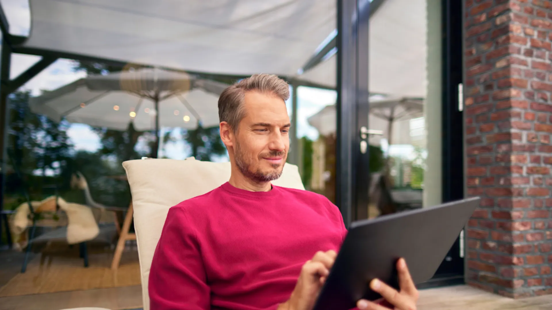 Produktwelt der NEW Ein Mann sitzt auf einem Gartenstuhl mit einem Tablet in der Hand und informiert sich über die Produktwelt der NEW.