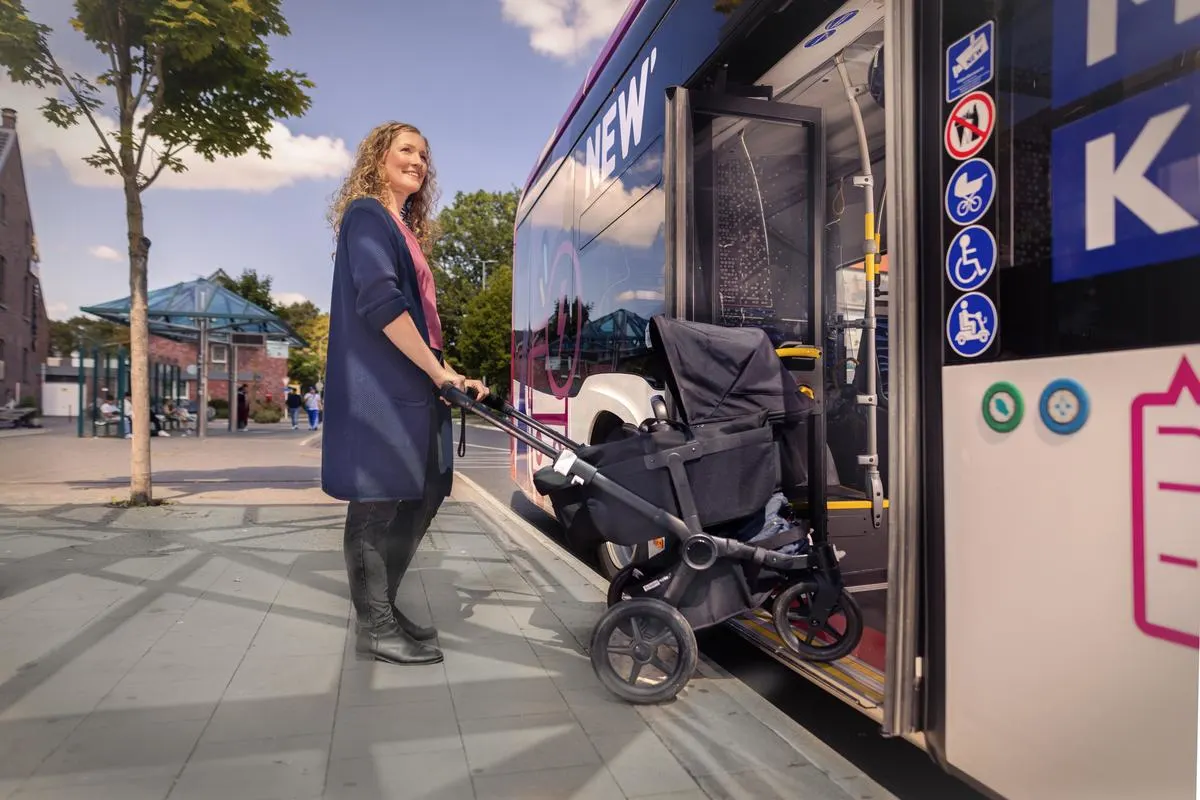 Weiblicher Fahrgast mit Kinderwagen beim zusteigen.