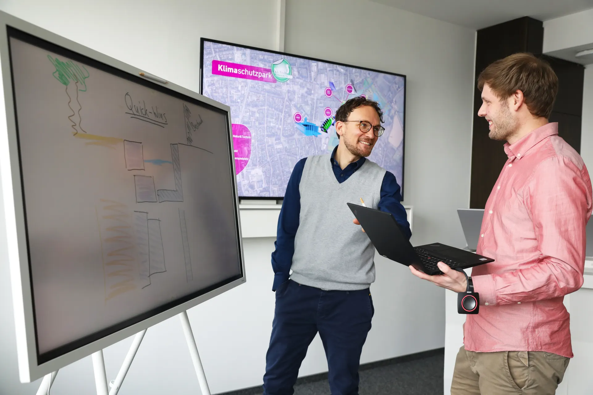 Zwei Kollegen unterhalten sich vor einem digitalen Whiteboard