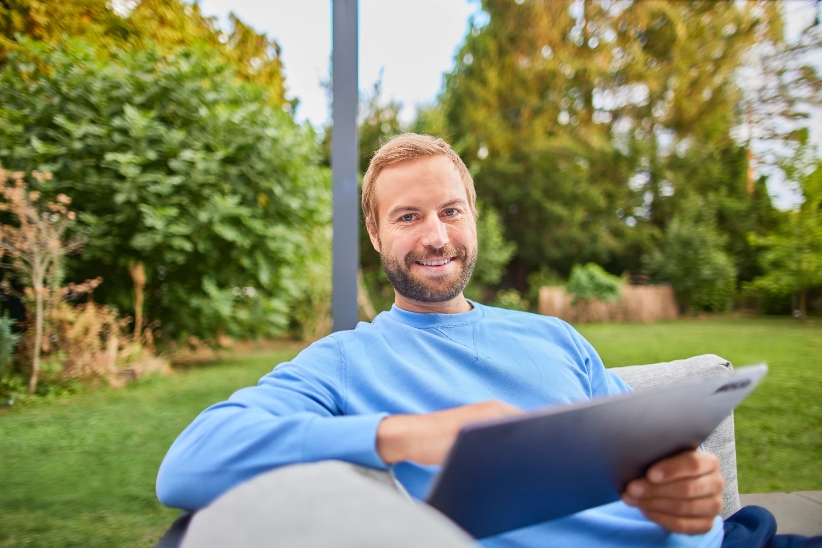 Ein Mann sitzt mit einem Tablet im Garten und entdeckt die Tarife und Services der NEW.