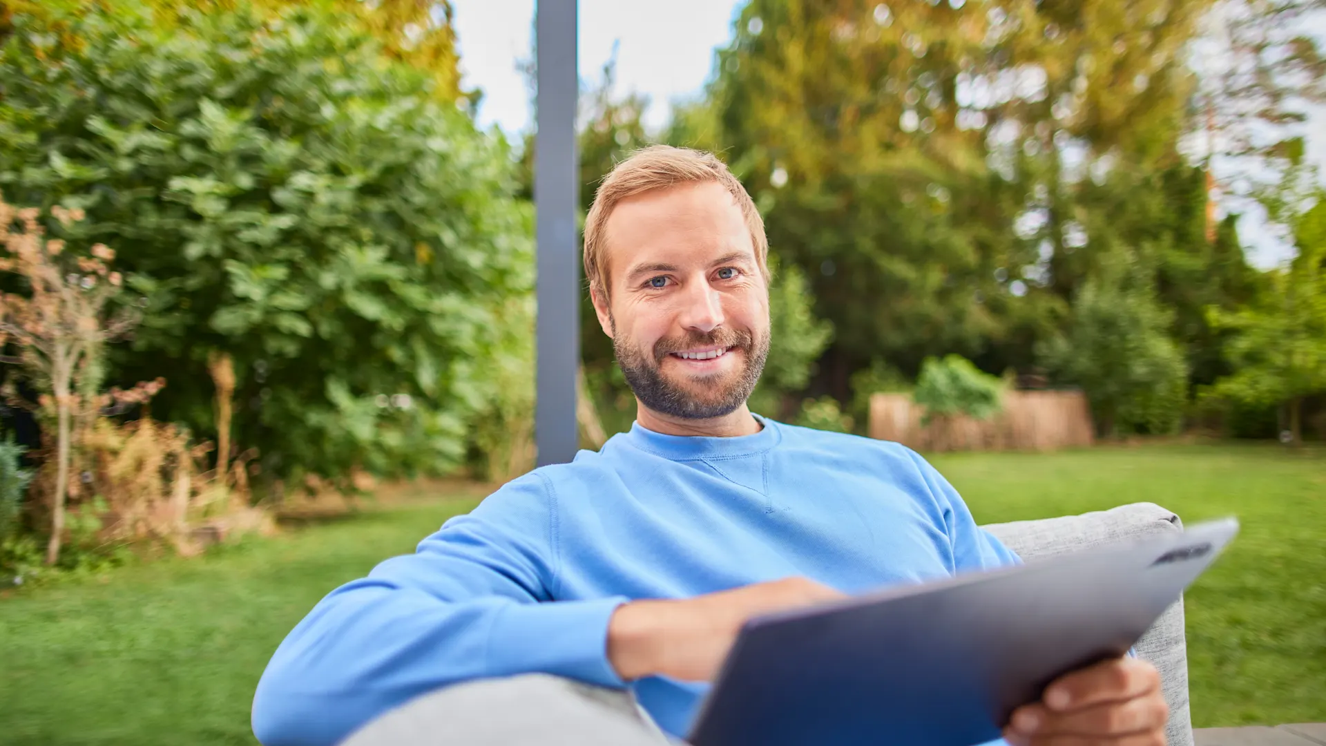NEW Services entdecken Ein Mann sitzt mit einem Tablet im Garten und entdeckt die Tarife und Services der NEW.