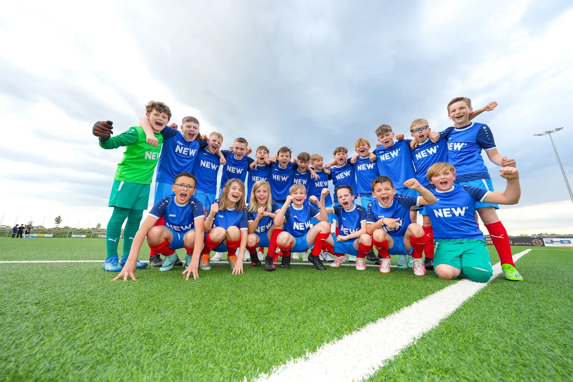 Eine Gruppe von jungen Fußballspielern stehen jubelnd auf einem Spielfeld, die Arme um die Schultern gelegt.