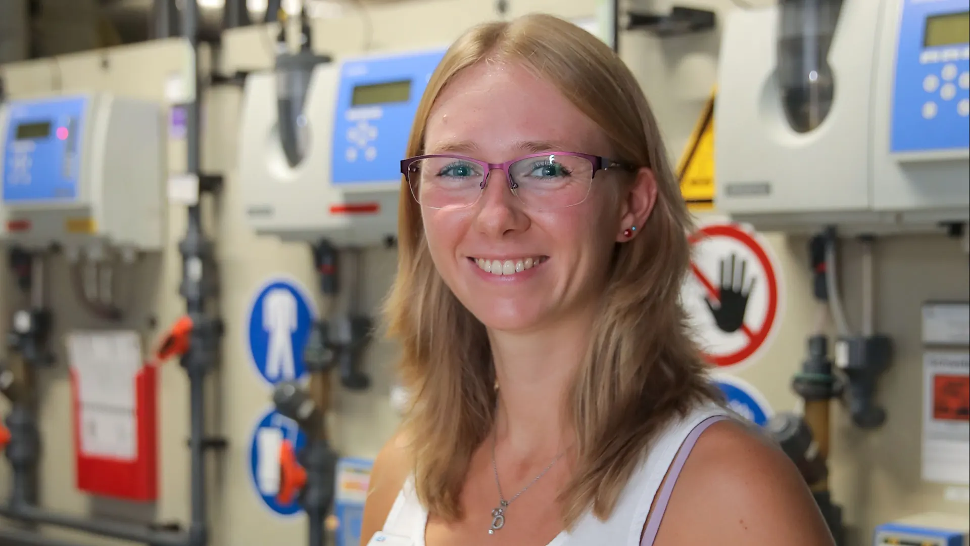 Jessica Wollmer schaut lächelnd in die Kamera. Sie steht in einem Technikraum.