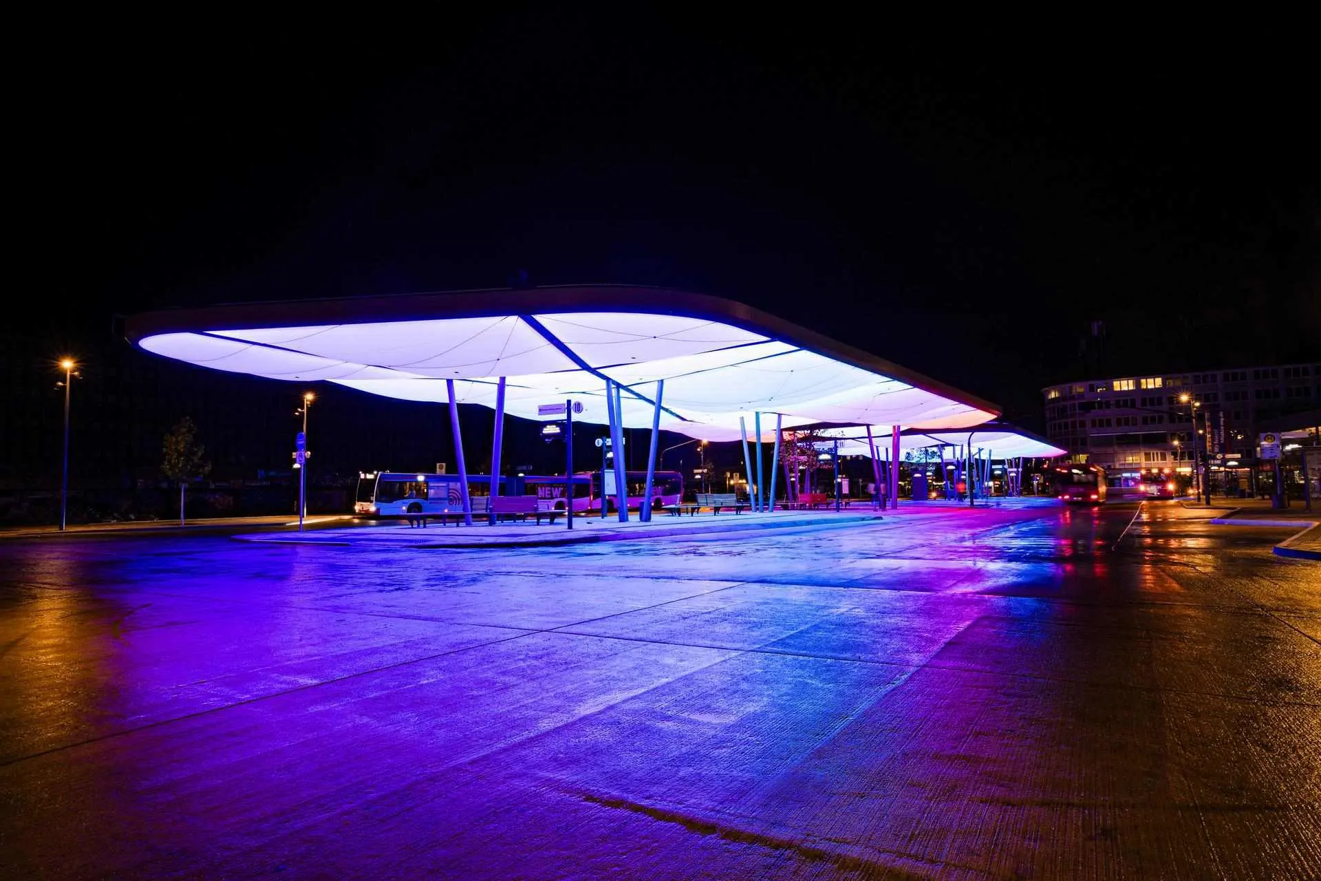 Das Bild zeigt den Zentralen Omnibusbahnhof (ZOB) in Mönchengladbach bei Nacht. Die moderne Dachkonstruktion ist farbig beleuchtet und prägt das Stadtbild. 