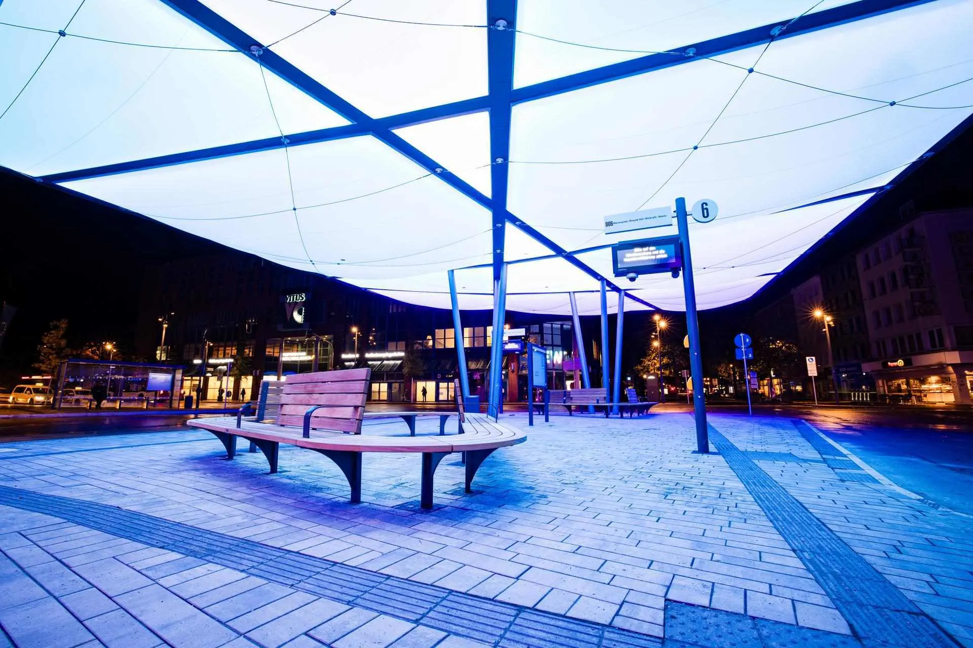 Beleuchteter ZOB in Mönchengladbach bei Nacht – mit geschwungener Sitzbank und hellblau strahlender Dachkonstruktion.