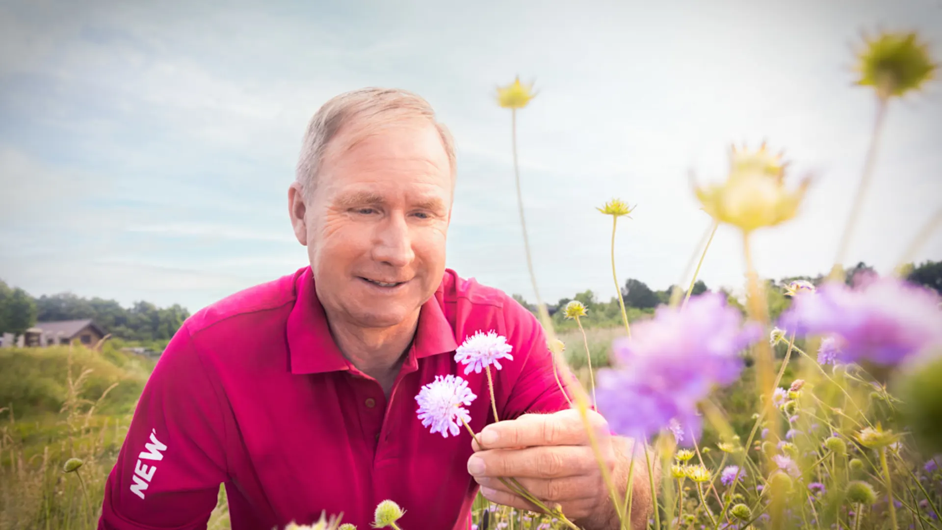 NEW-AG-Nachhaltigkeit Mann im NEW Poloshirt auf einer Wildwiese mit einer Blume in der Hand.