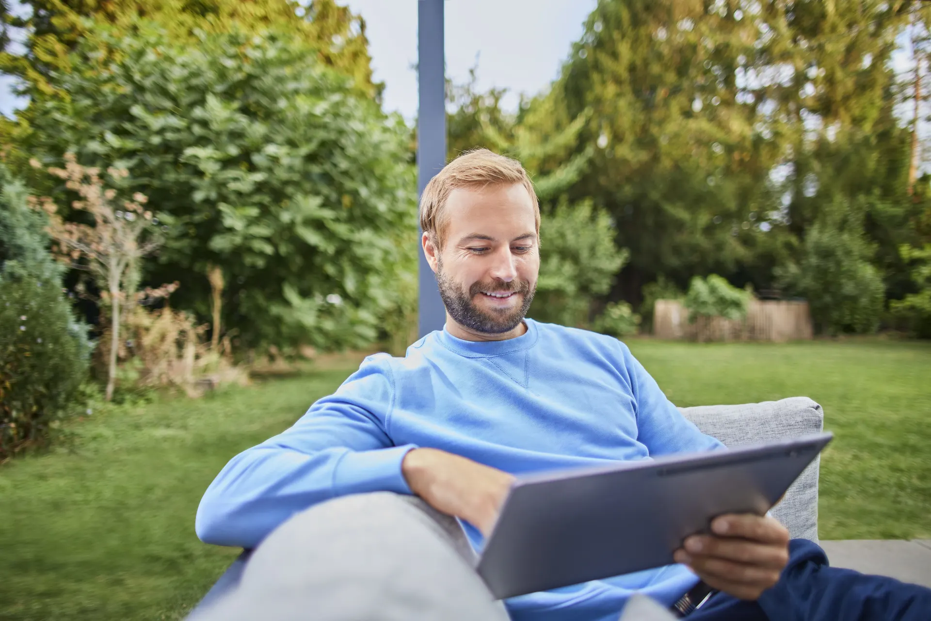 Mann sitzt im Garten und schaut auf sein Tablet.