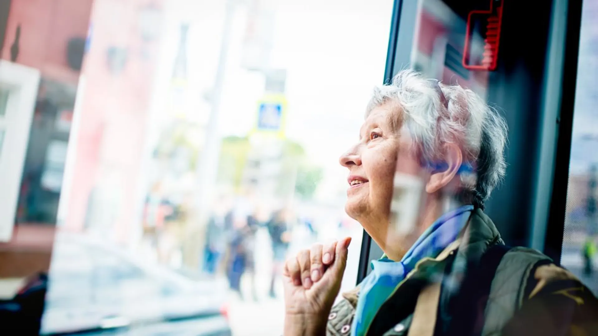 Ohne Auto mobil Ältere Dame im Bus, wie sie aus dem Fenster schaut.