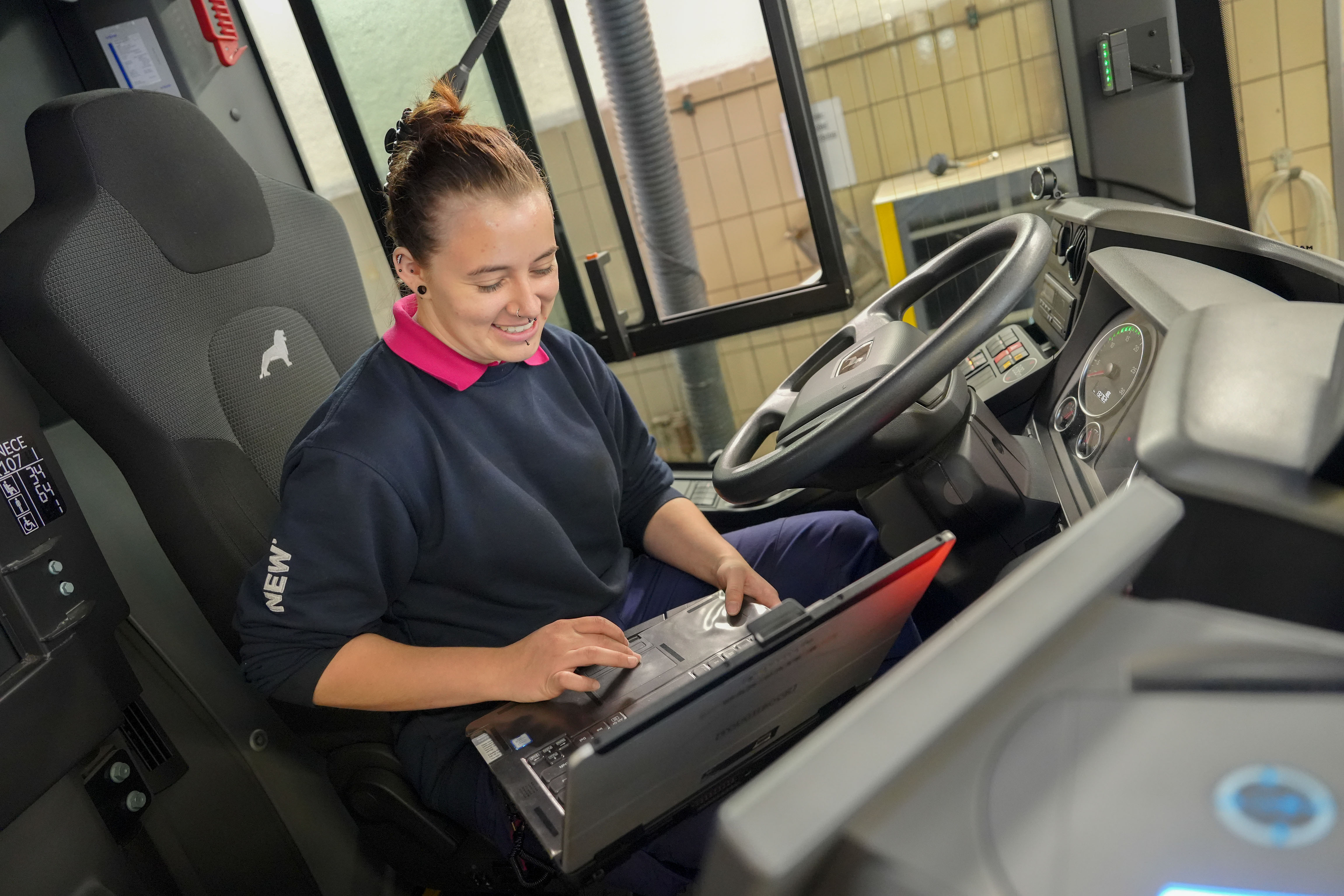 Daniela Albers, Auszubildende zur Kfz-Mechatronikerin, sitzt auf dem Fahrersitz eines stehenden Fahrzeugs und arbeitet an einem Laptop.